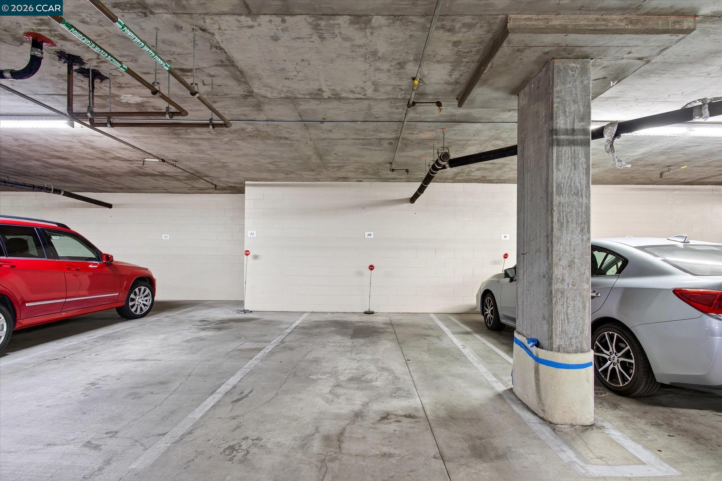 Underground parking garage with marked spaces, exposed pipes, and a concrete support column.