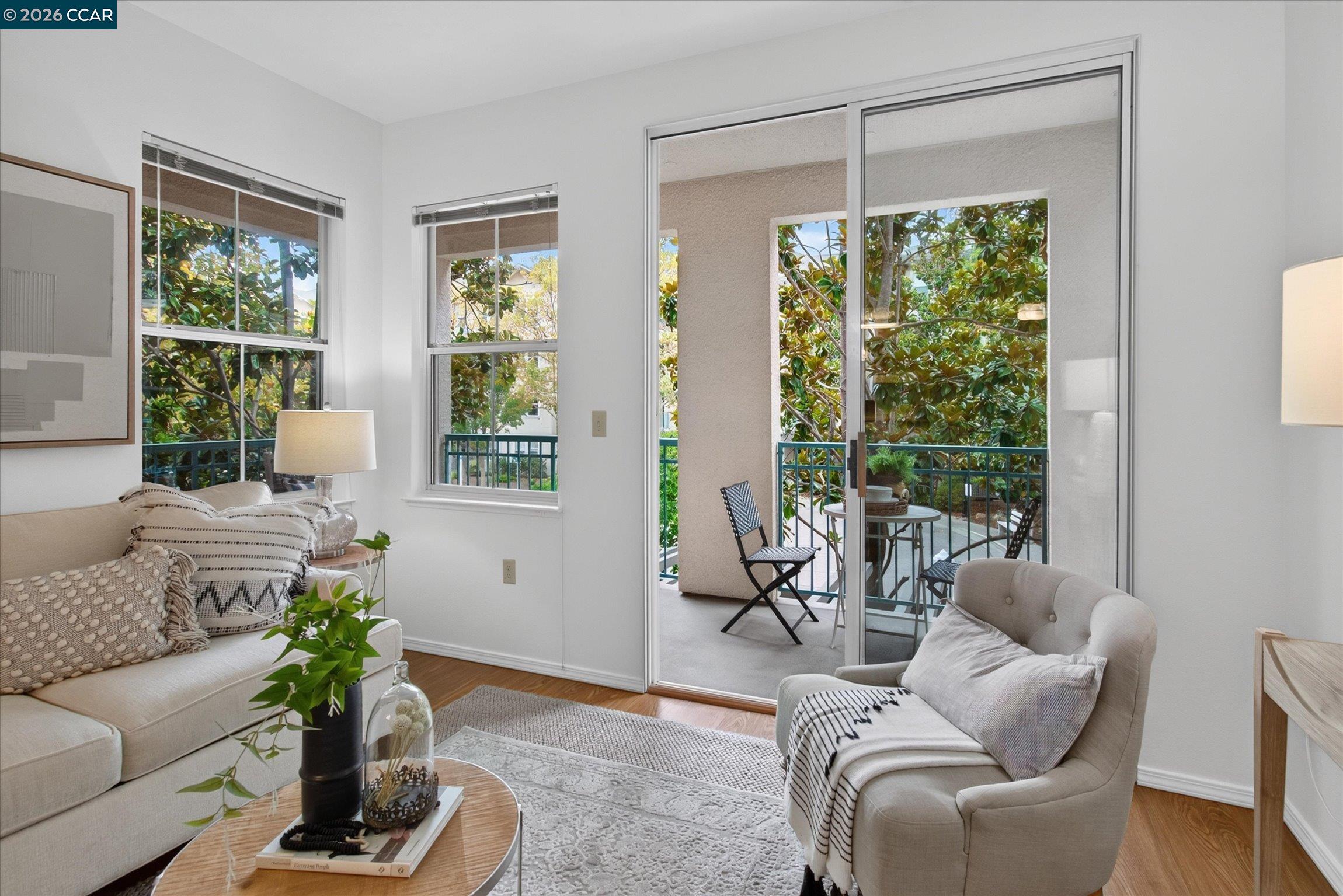 Living room with light sofas and large windows opening onto a leafy balcony.