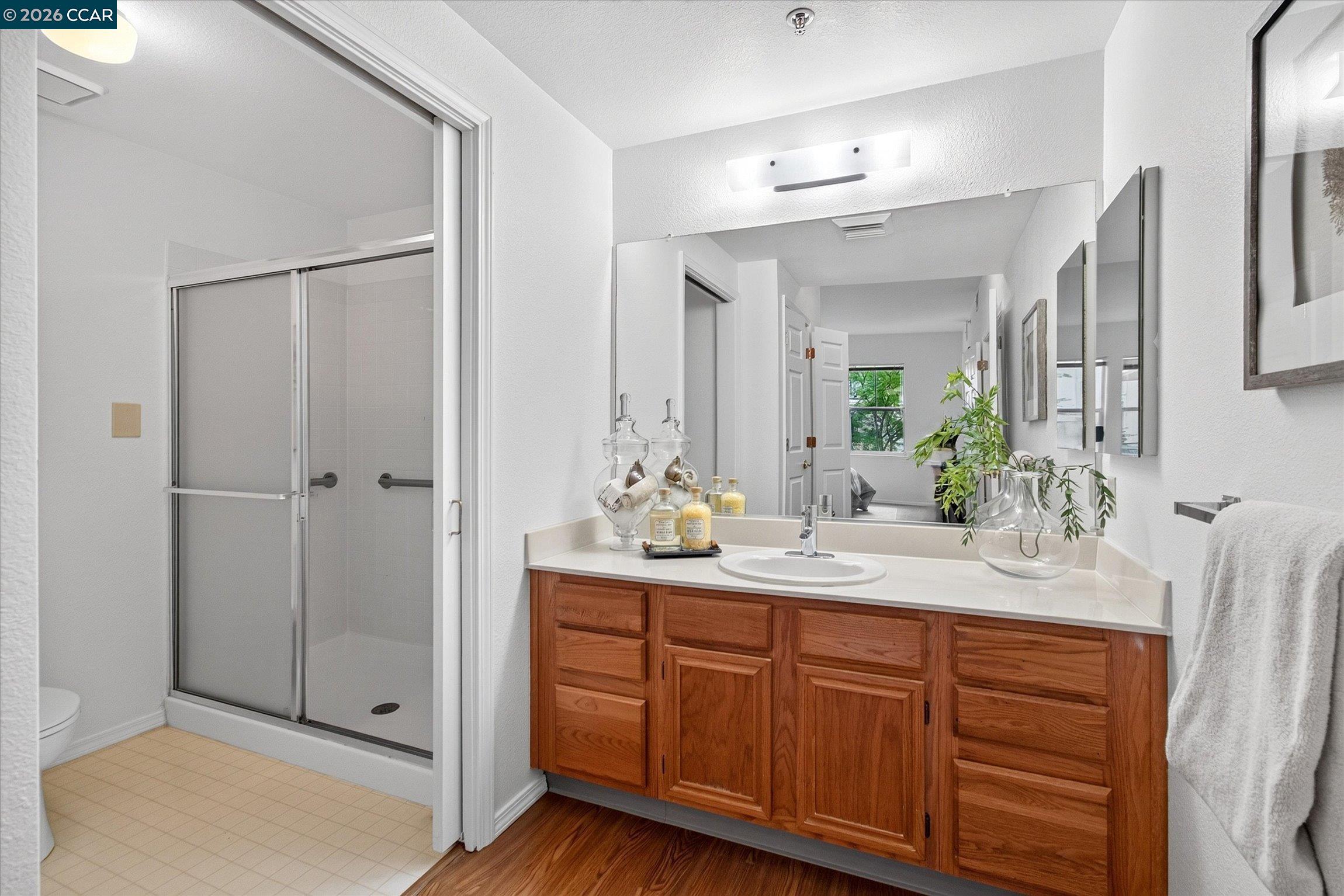 Bathroom with a wood vanity, large mirror and glass-enclosed shower.