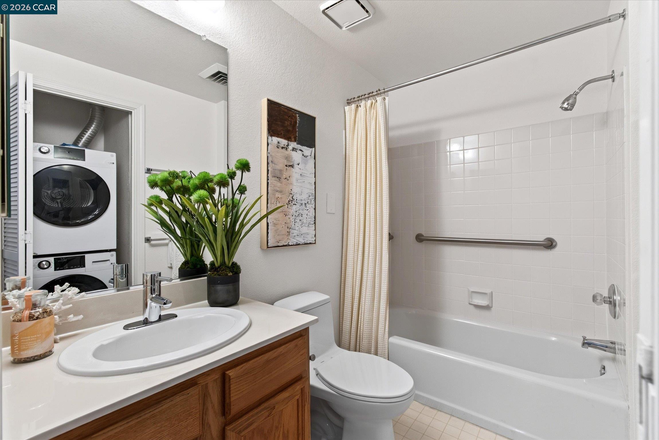 Bathroom with tiled tub and grab bar, wood vanity, and stacked washer and dryer.