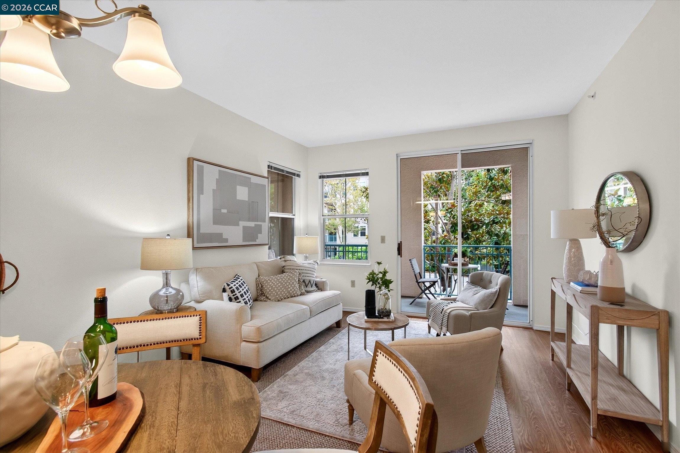 Staged living room with cream seating and sliding doors opening to a leafy balcony.
