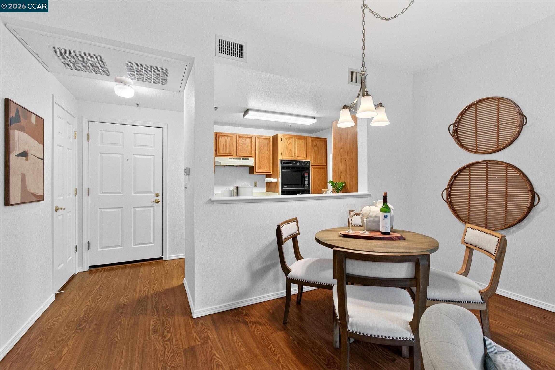 Dining area with a round table and white chairs beside an open kitchen and entry.