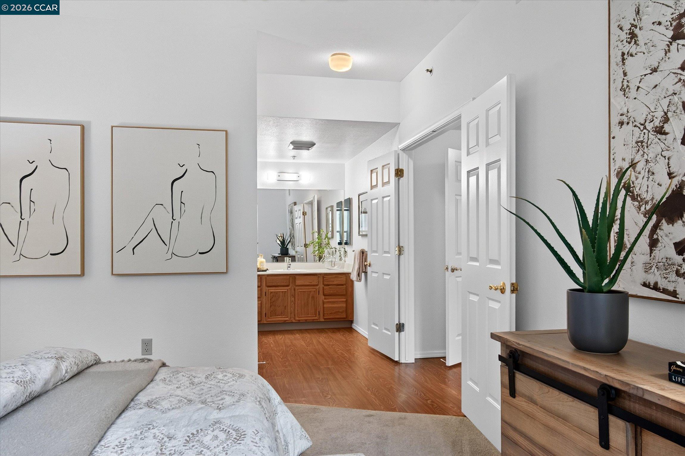 Furnished bedroom with open doors revealing a bathroom and wood vanity.