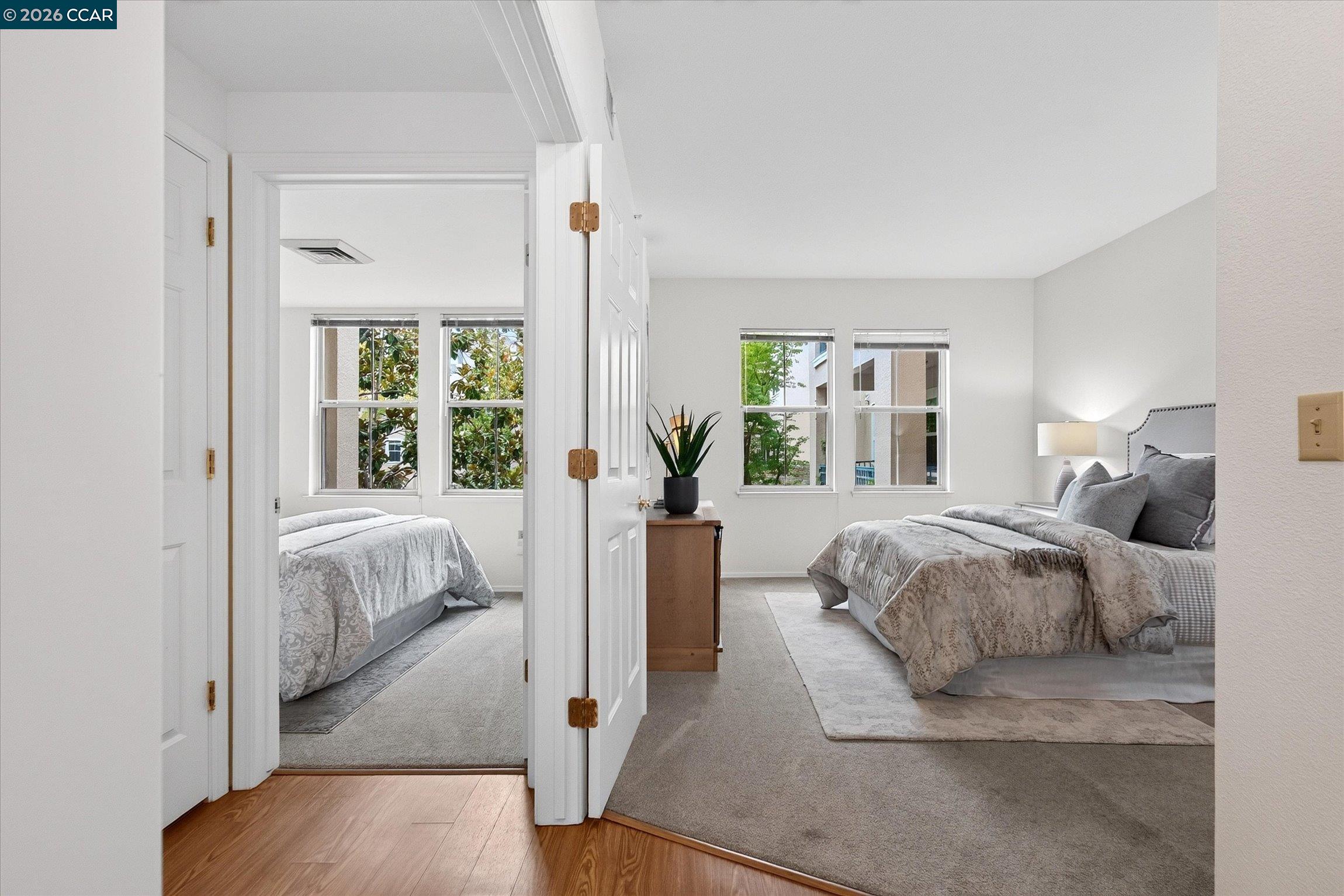 Two staged bedrooms, with a gray bed in the foreground room and another bed visible through the doorway.