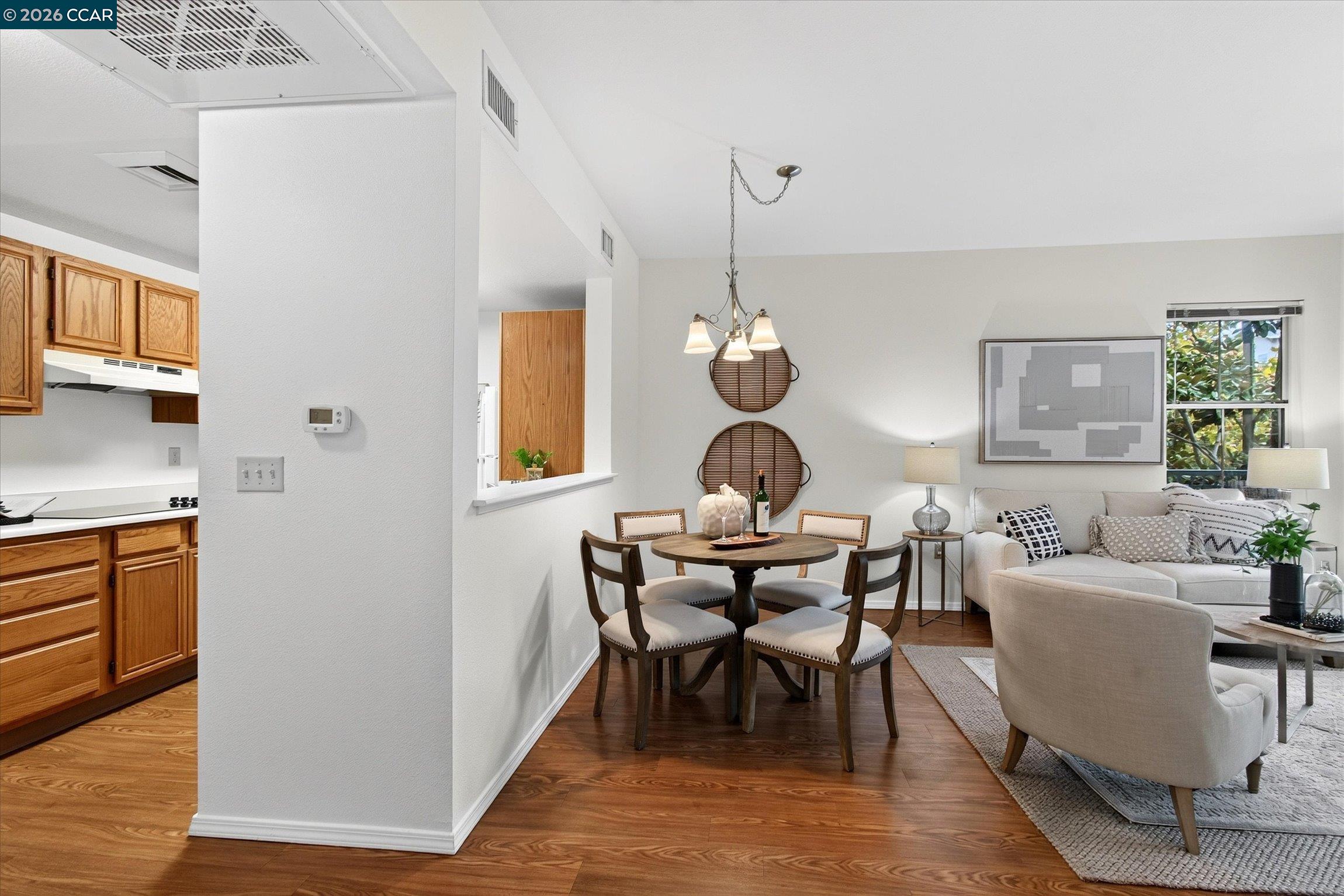 Open-plan dining and living area with a round table, light sectional, and warm wood floors.