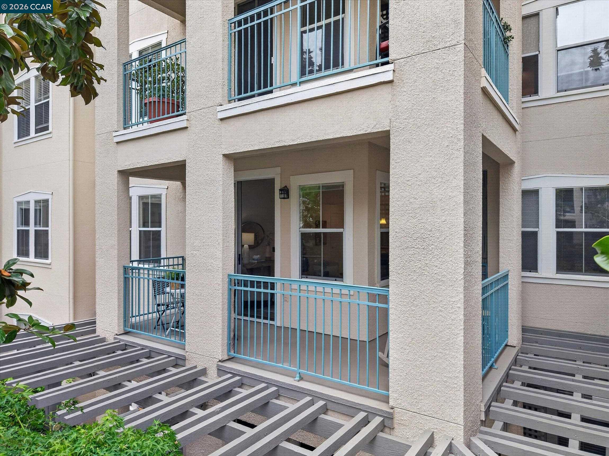 Condominium exterior with blue-railed balconies and a gray pergola in the foreground.