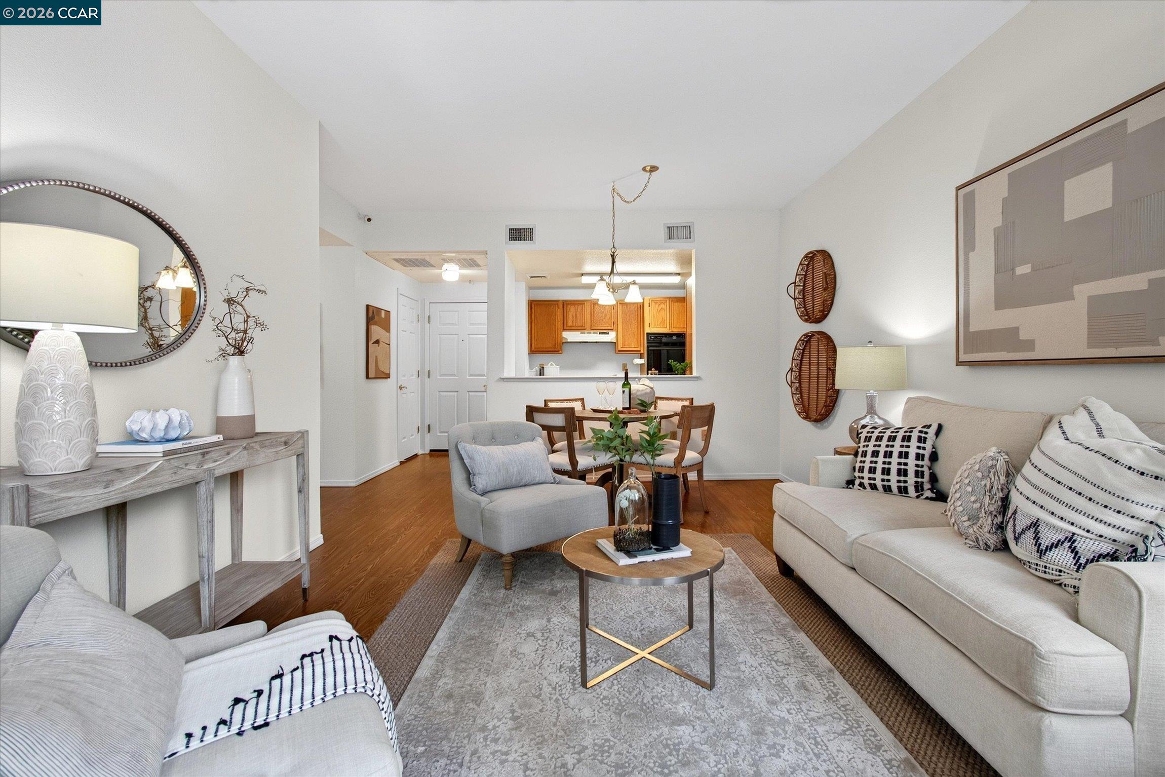 Staged living and dining area with light sofas, wood flooring, and an open kitchen.