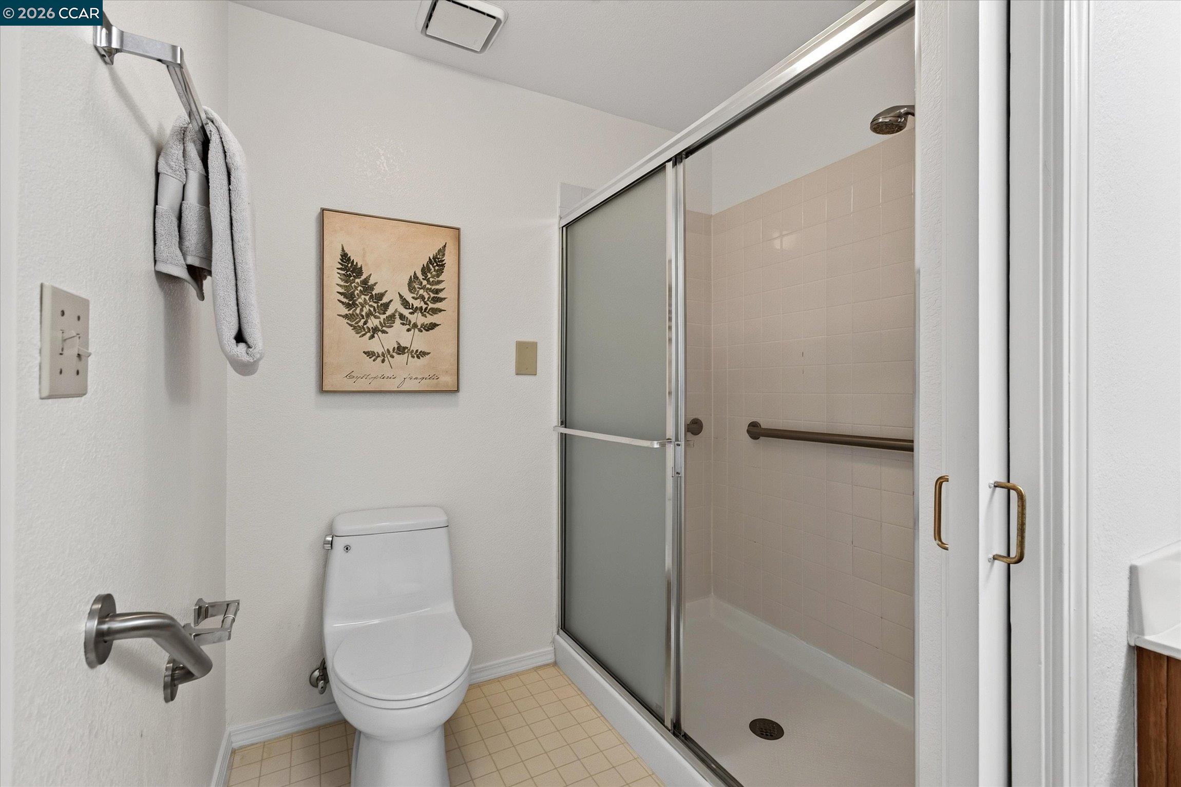 Bathroom with a toilet and tiled shower enclosure featuring grab bars and frosted sliding doors.