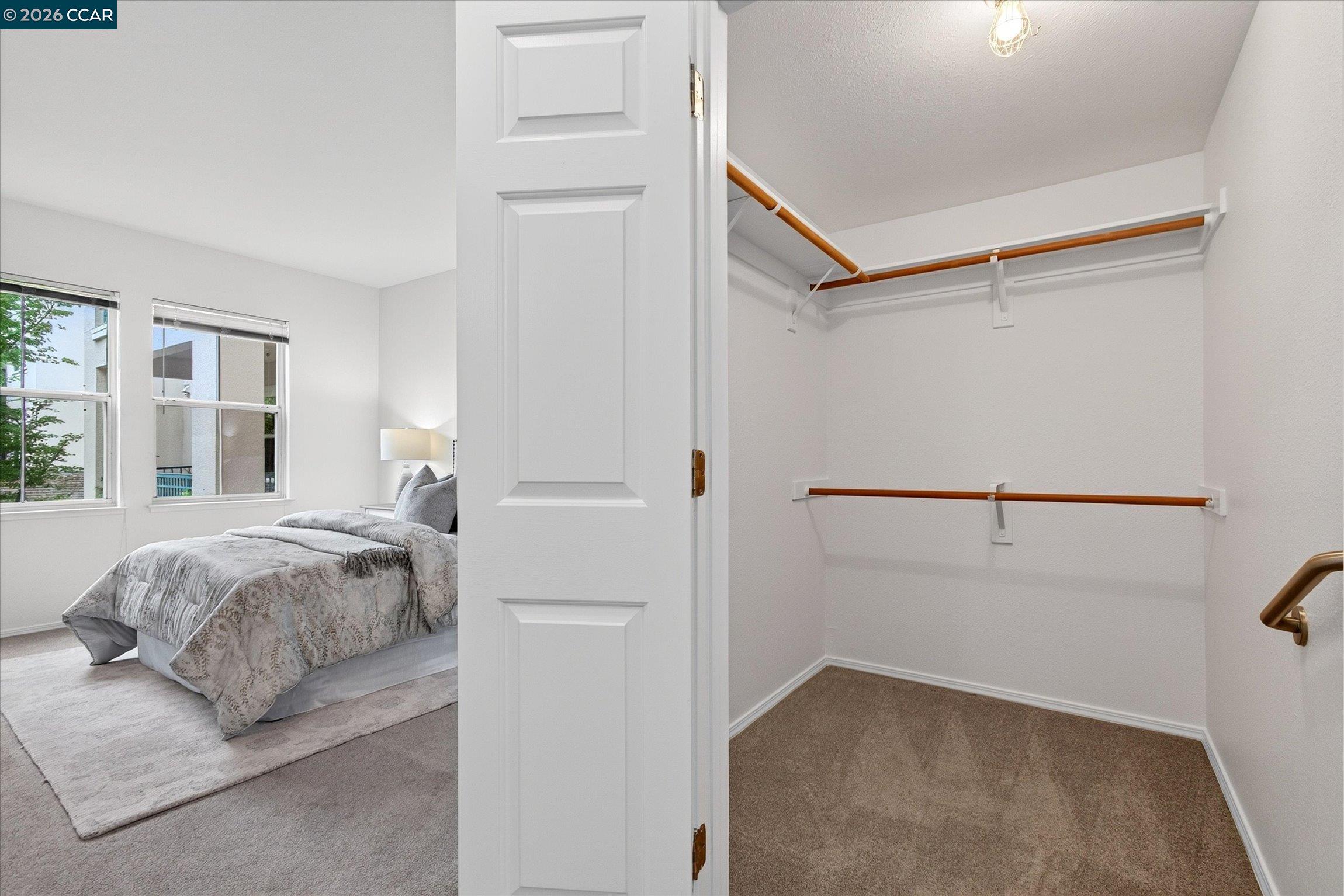 Furnished bedroom beside a spacious walk-in closet with wood-toned hanging rods.