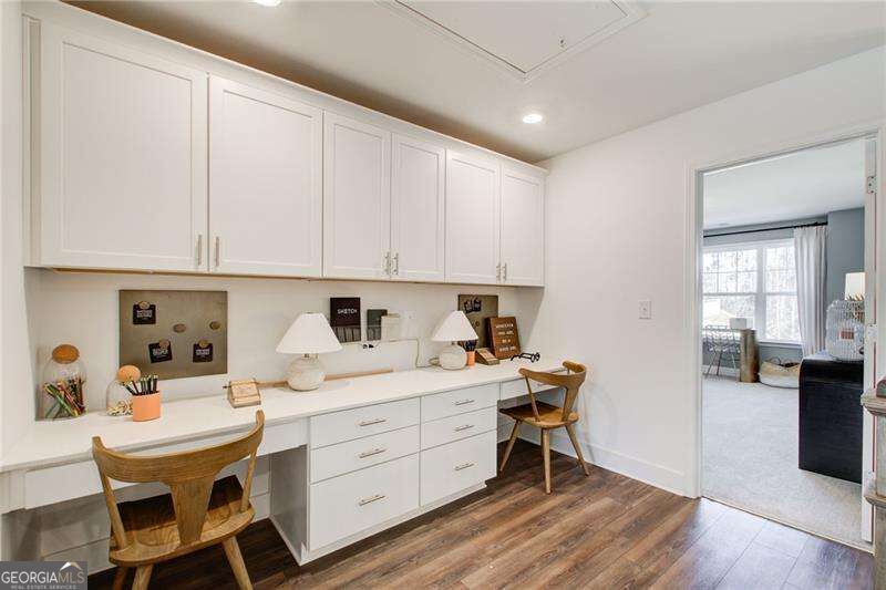 Home office with a built-in white desk, extensive cabinetry, and two wooden chairs.