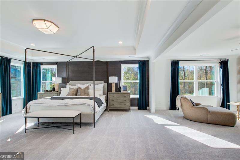 Bright primary bedroom with a four-poster bed, teal curtains, and a window-side sitting area.