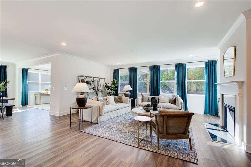 Living room with light sofas, large curtained windows, wood floors, and a fireplace.