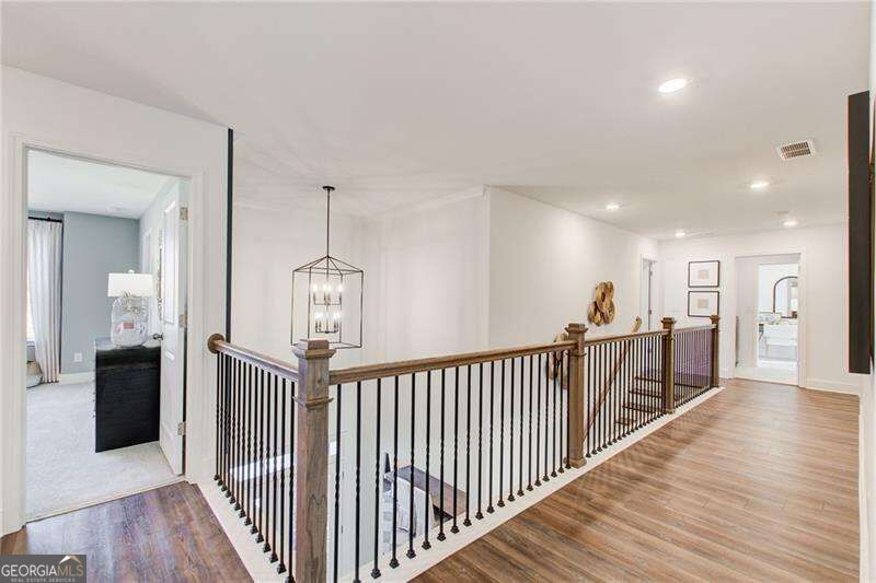 Upstairs hallway overlooking an open staircase with black balusters, a wood handrail, and wood-look floors.