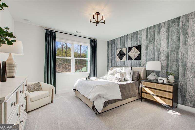 Staged bedroom with a gray accent wall, geometric artwork, and a large bed beneath a window.