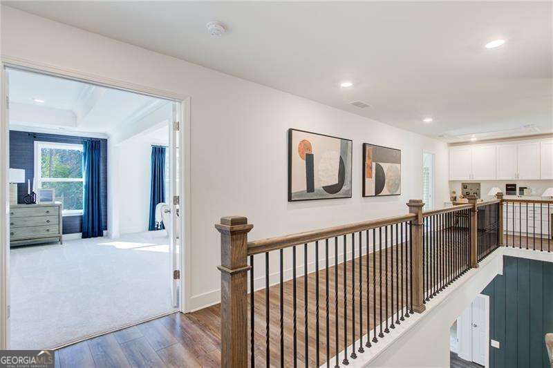 Upstairs landing with hardwood floors, framed art, and a dark metal railing overlooking the lower level.
