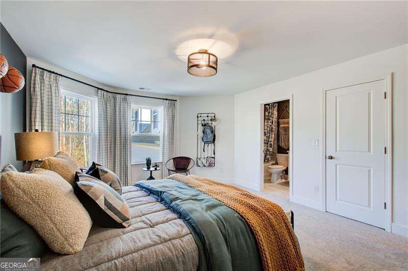 Furnished bedroom with layered bedding, tall curtained windows, and an open doorway to the bathroom.