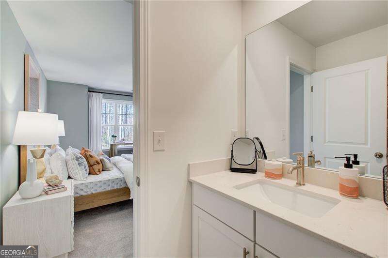 Bathroom vanity and mirror beside an open doorway to a bedroom with a bed.