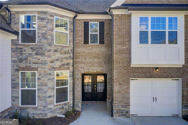 Two-story stone-and-brick home with a dark entry, white-trimmed windows, and an attached garage.