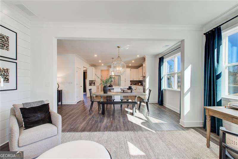 Open-plan living and dining area with a chandelier, dark wood floors, and large windows with blue curtains.