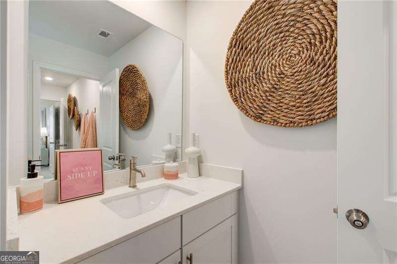 Bathroom vanity with a white countertop, chrome faucet, large mirror, and round woven wall decoration.