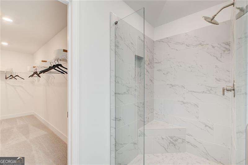 Marble-look tiled shower with glass enclosure and built-in bench beside an open walk-in closet.