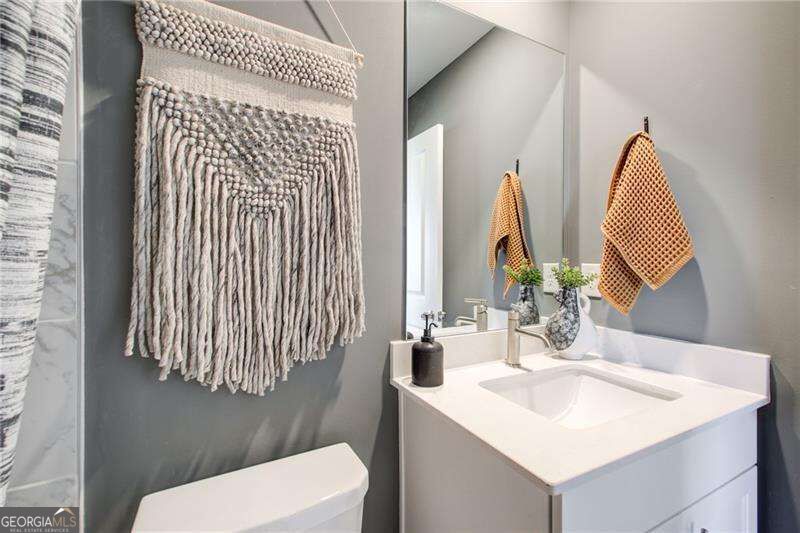 Bathroom vanity with a white sink, large mirror, gray walls, and woven wall hangings.