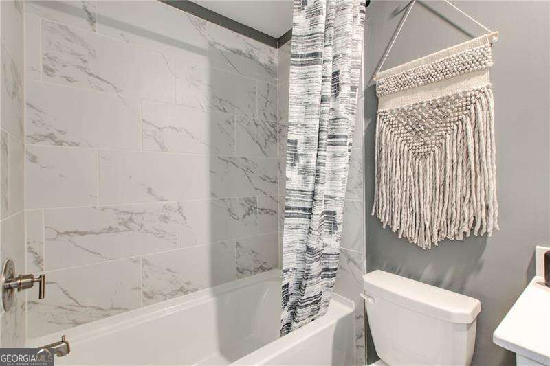Bathroom with a marble-look tiled tub surround, striped shower curtain, and woven wall hanging.