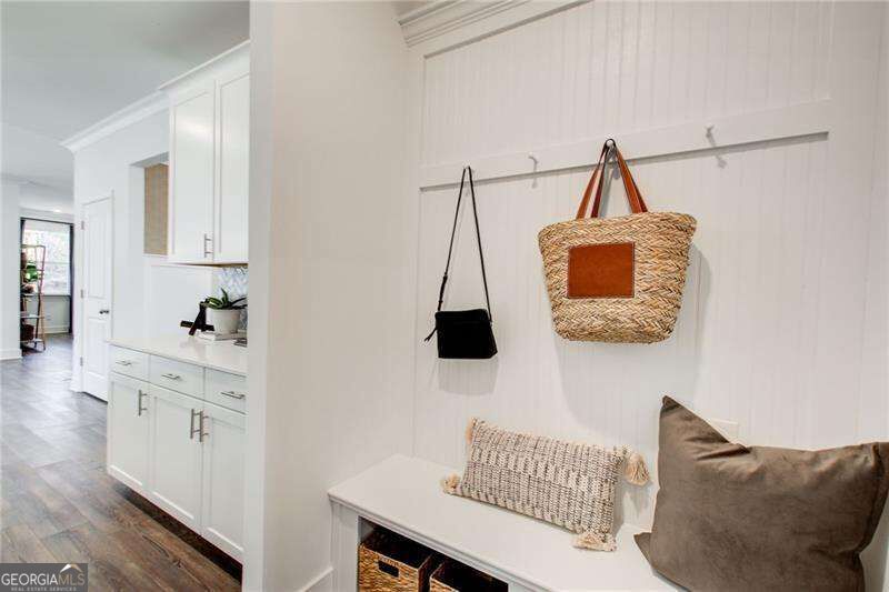 White mudroom bench with handbags on wall hooks and woven baskets below.
