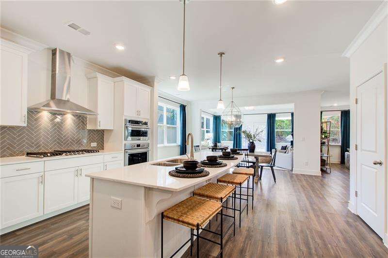 Open-plan kitchen with a white island, woven-seat stools, and gray herringbone backsplash.