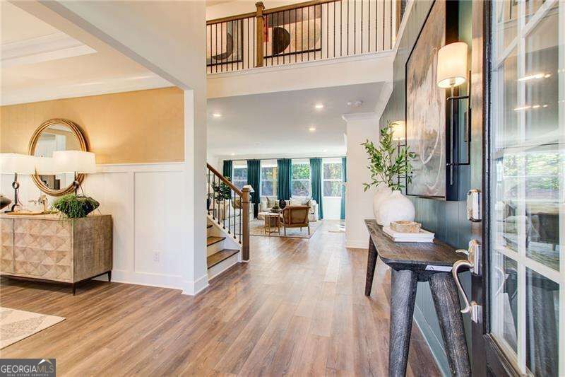 Two-story entry foyer with warm wood floors, a staircase, and a console table beside tall windows.