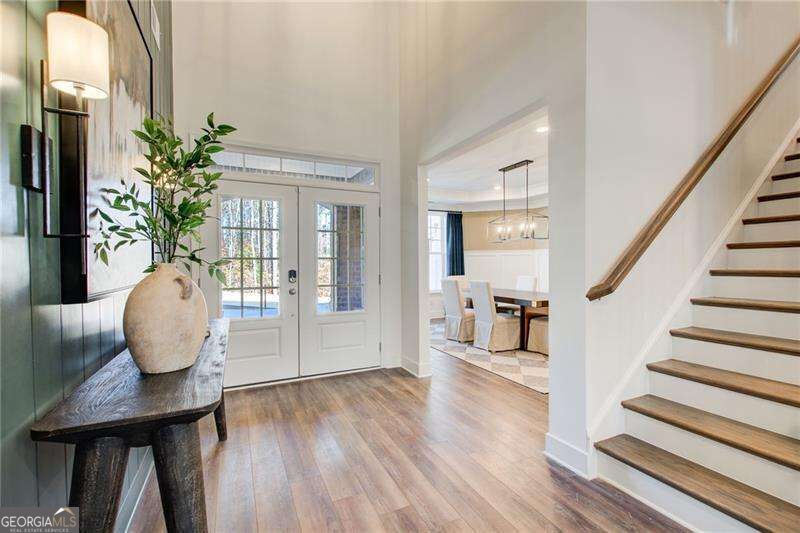 Entry foyer with double doors, hardwood floors, a console table, and staircase.