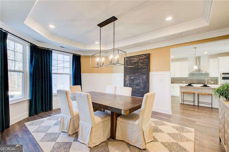 Dining room with a dark wood table, cream chairs, and a glass chandelier beside an open kitchen.