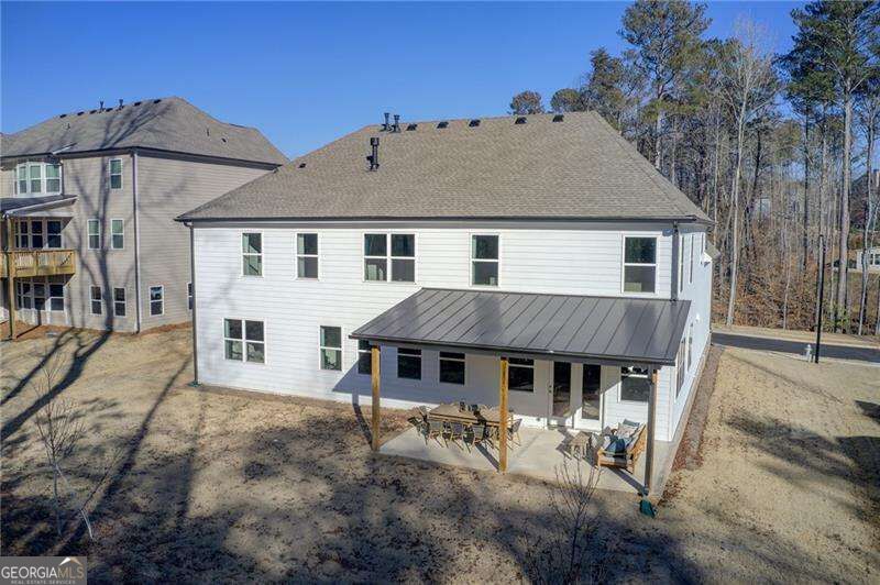 Rear exterior of a white two-story home with a covered patio and wooded backdrop.