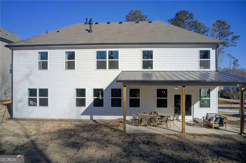 Rear of a white two-story house with a covered, furnished patio and bare yard.