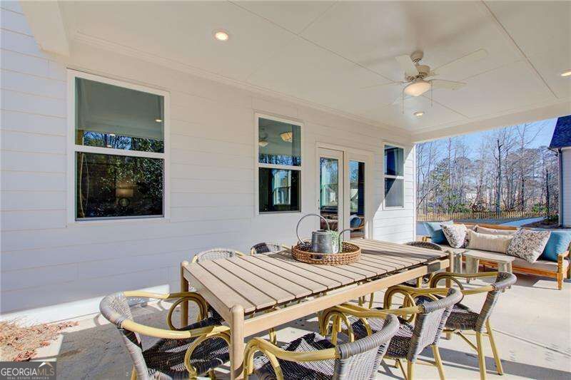Covered patio with an outdoor dining set, ceiling fan, and cushioned seating overlooking a fenced yard.