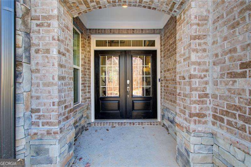 Covered brick entry with black double doors beneath an arched brick ceiling.