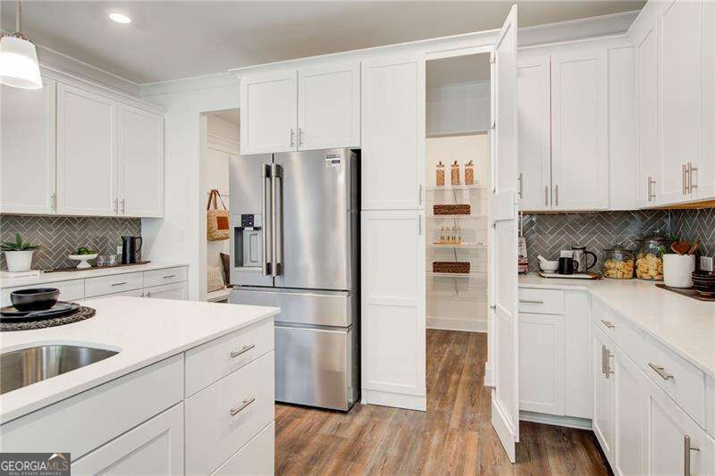 White kitchen with stainless steel appliances, a large island, and an open pantry.