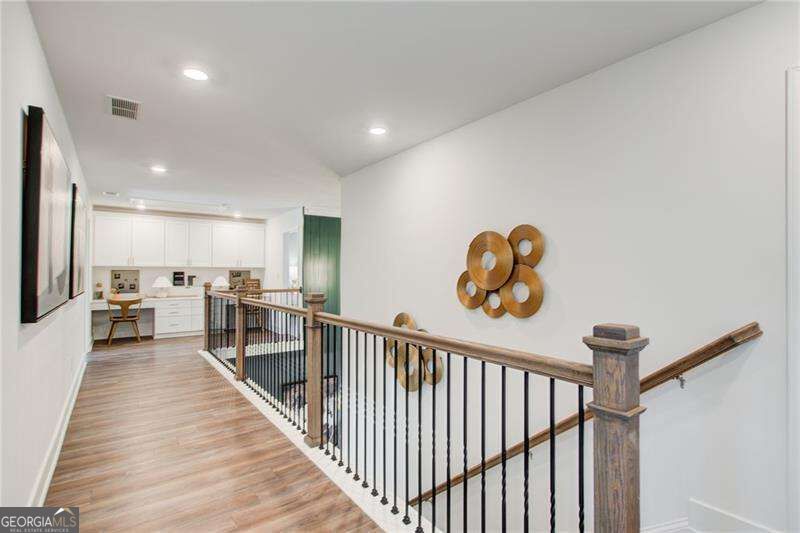 Upstairs landing with a black metal stair railing, wood-look flooring, and a small kitchen at the end.
