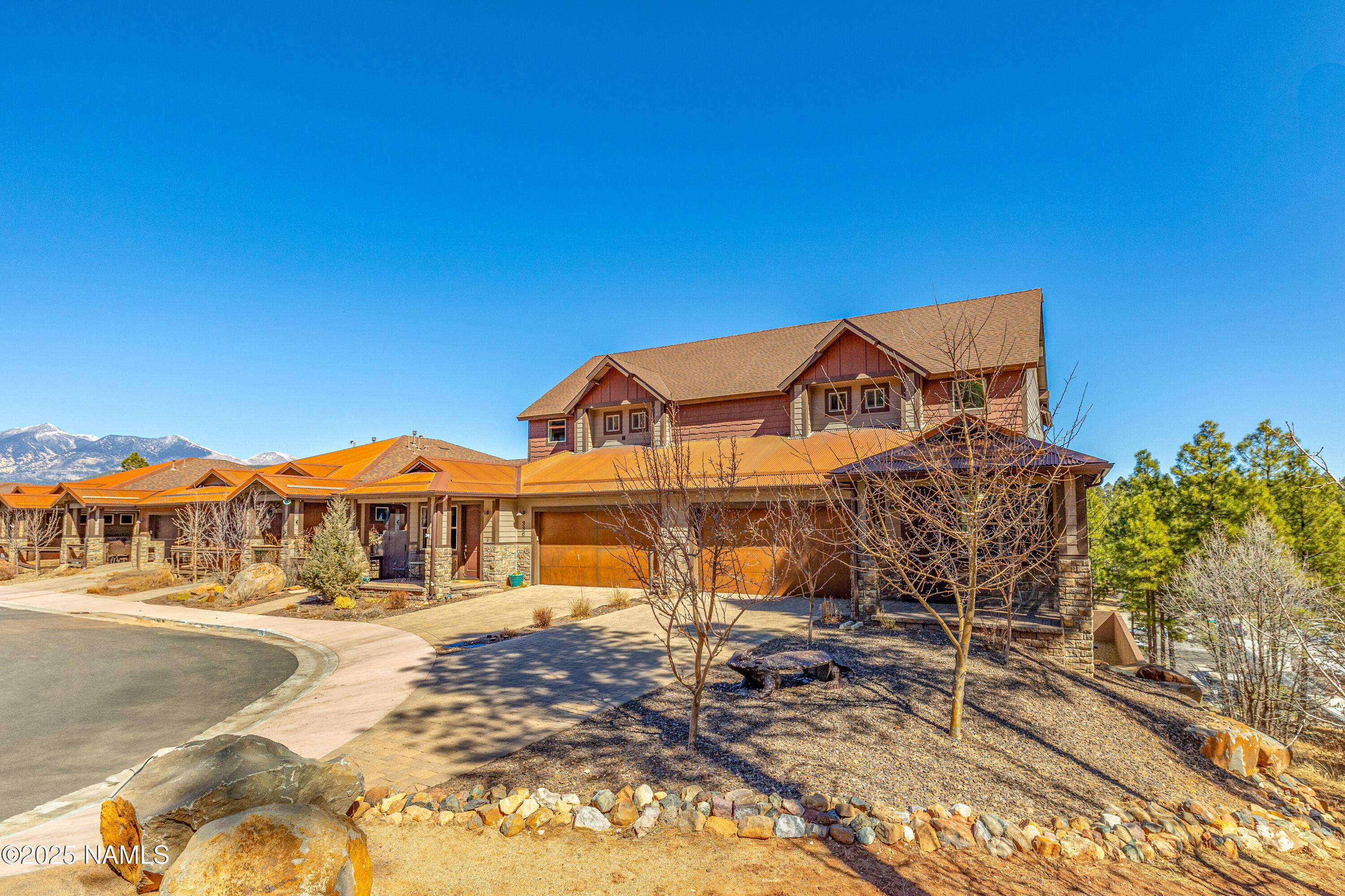 Two-story home with stone accents, warm-toned roofs, and mountains in the background.