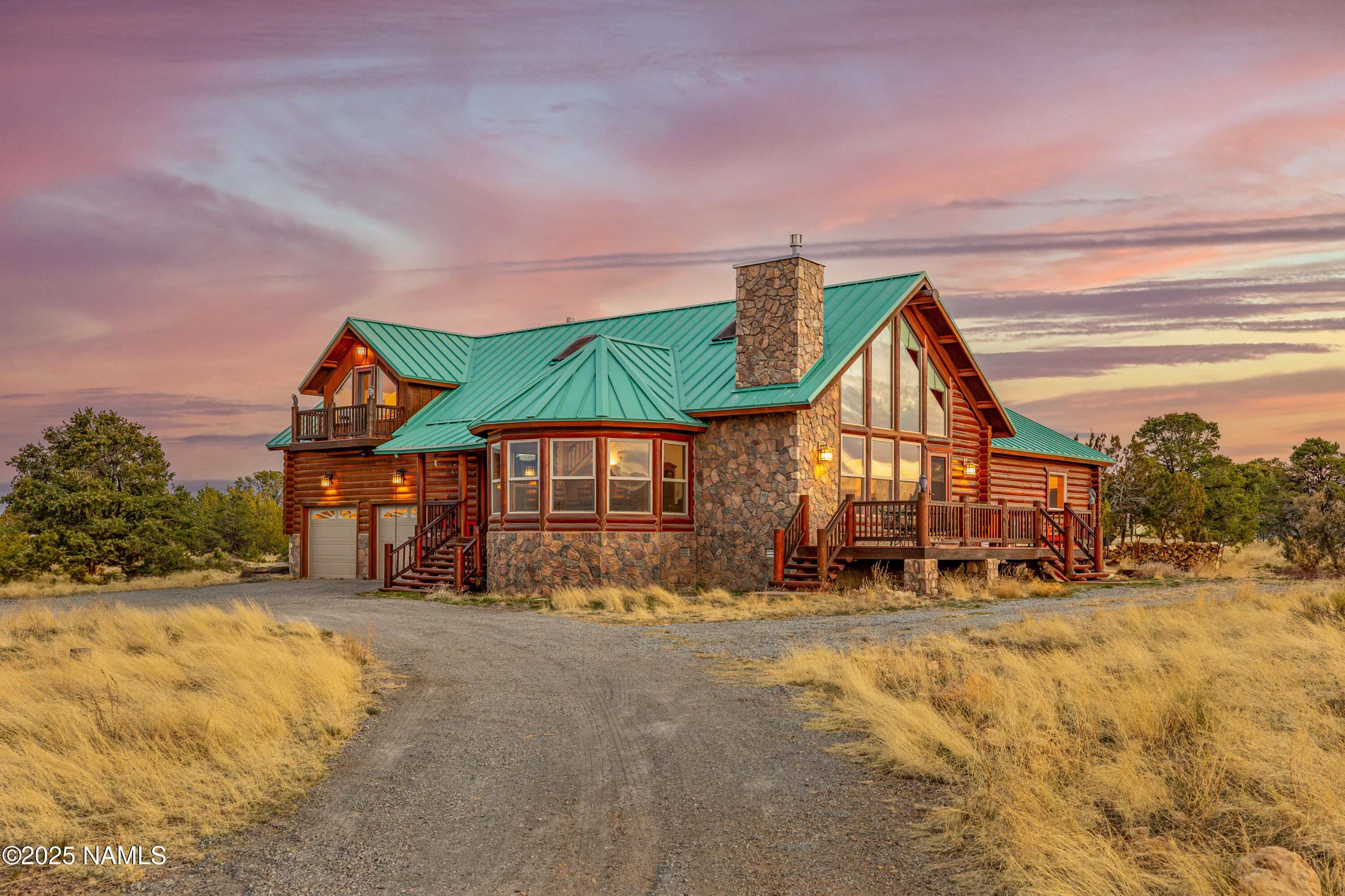 Log home with a green metal roof and stone chimney, photographed at sunset.