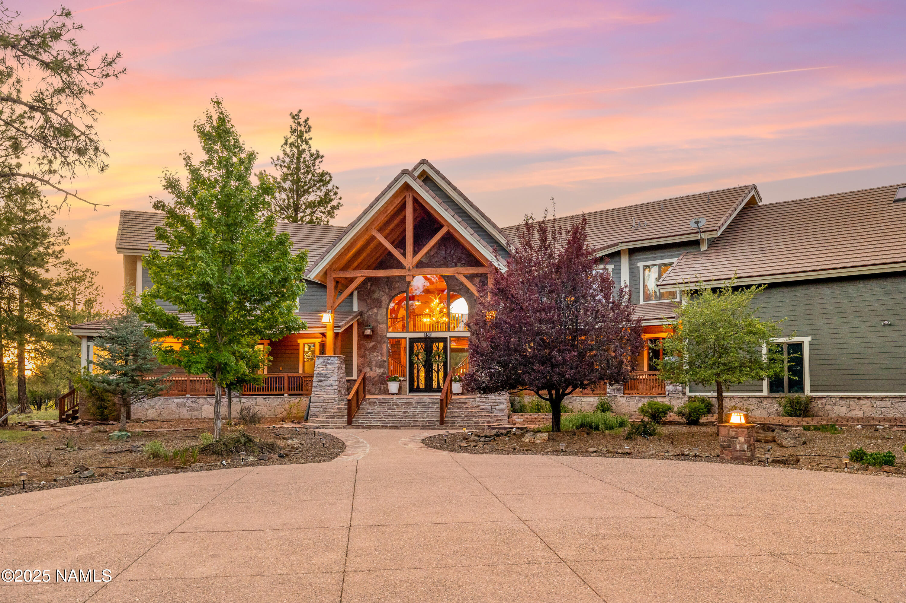 Large home with a timber-and-stone entrance, landscaped grounds, and a curved driveway at sunset.