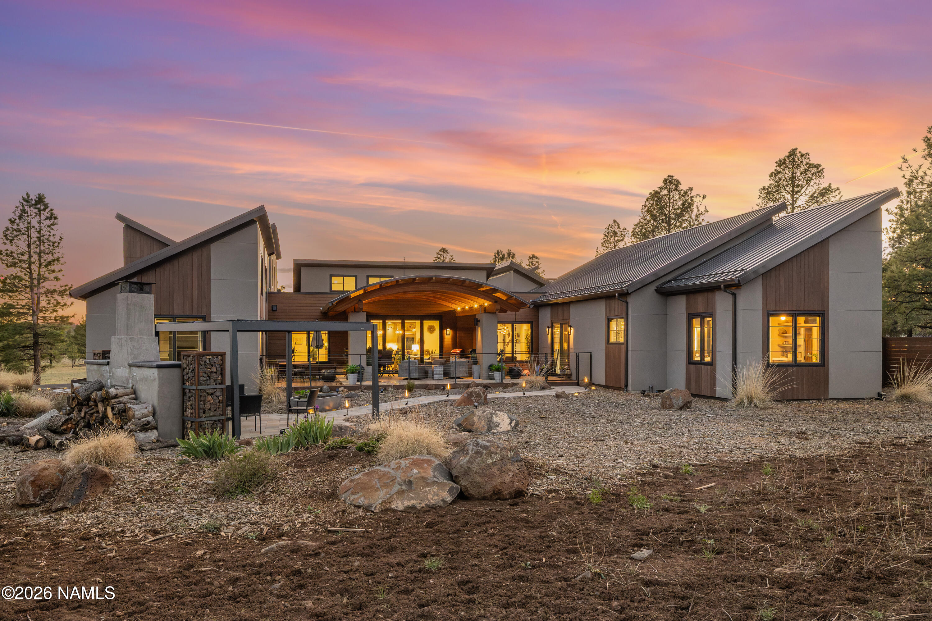Modern home with angular metal roofs and an illuminated covered patio at sunset.
