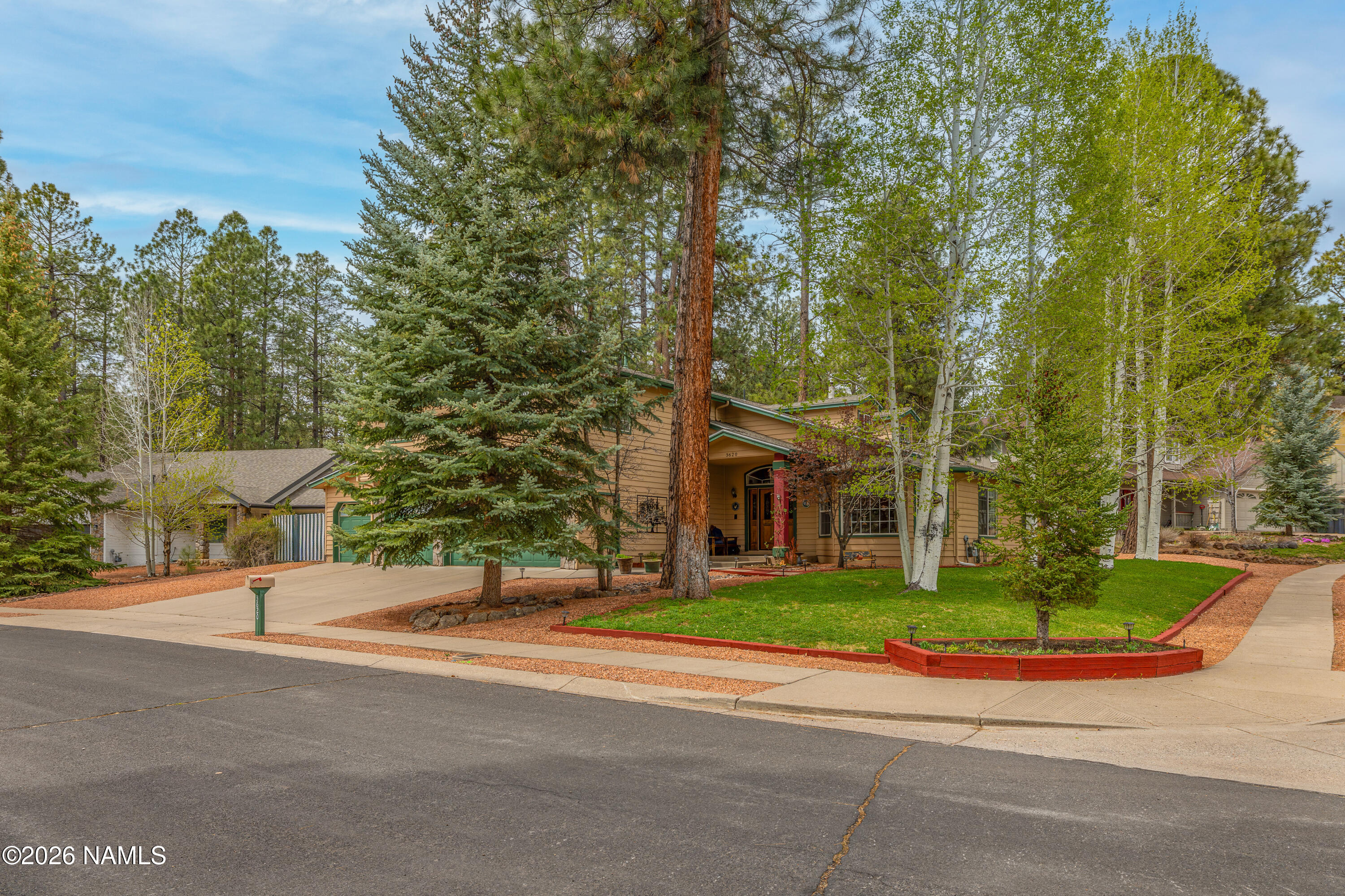Tan home with green trim, framed by tall pines and aspens and a landscaped front yard.