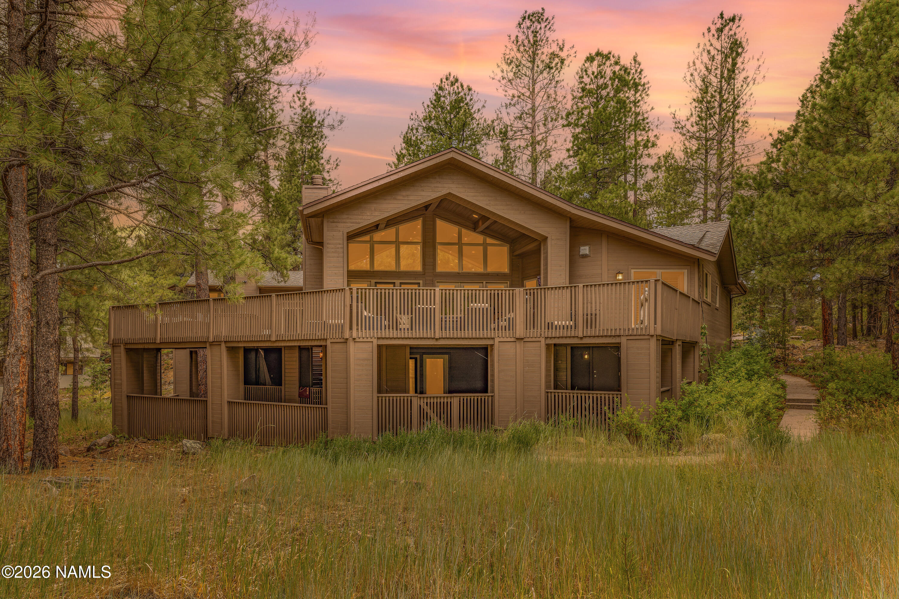 Wood-sided home with a broad deck among pine trees at dusk.