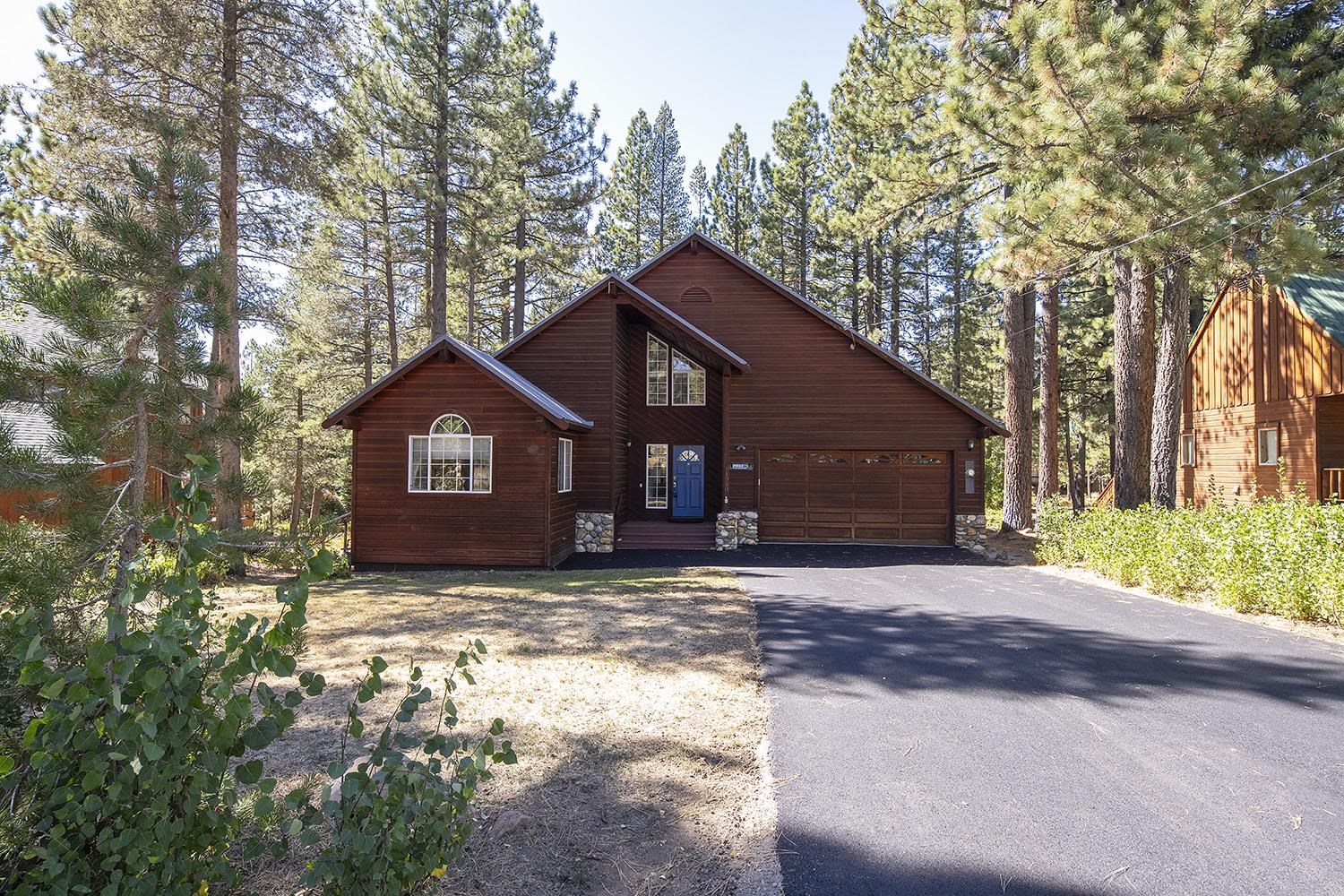 Wood-sided home with a blue front door and two-car garage among tall pine trees.