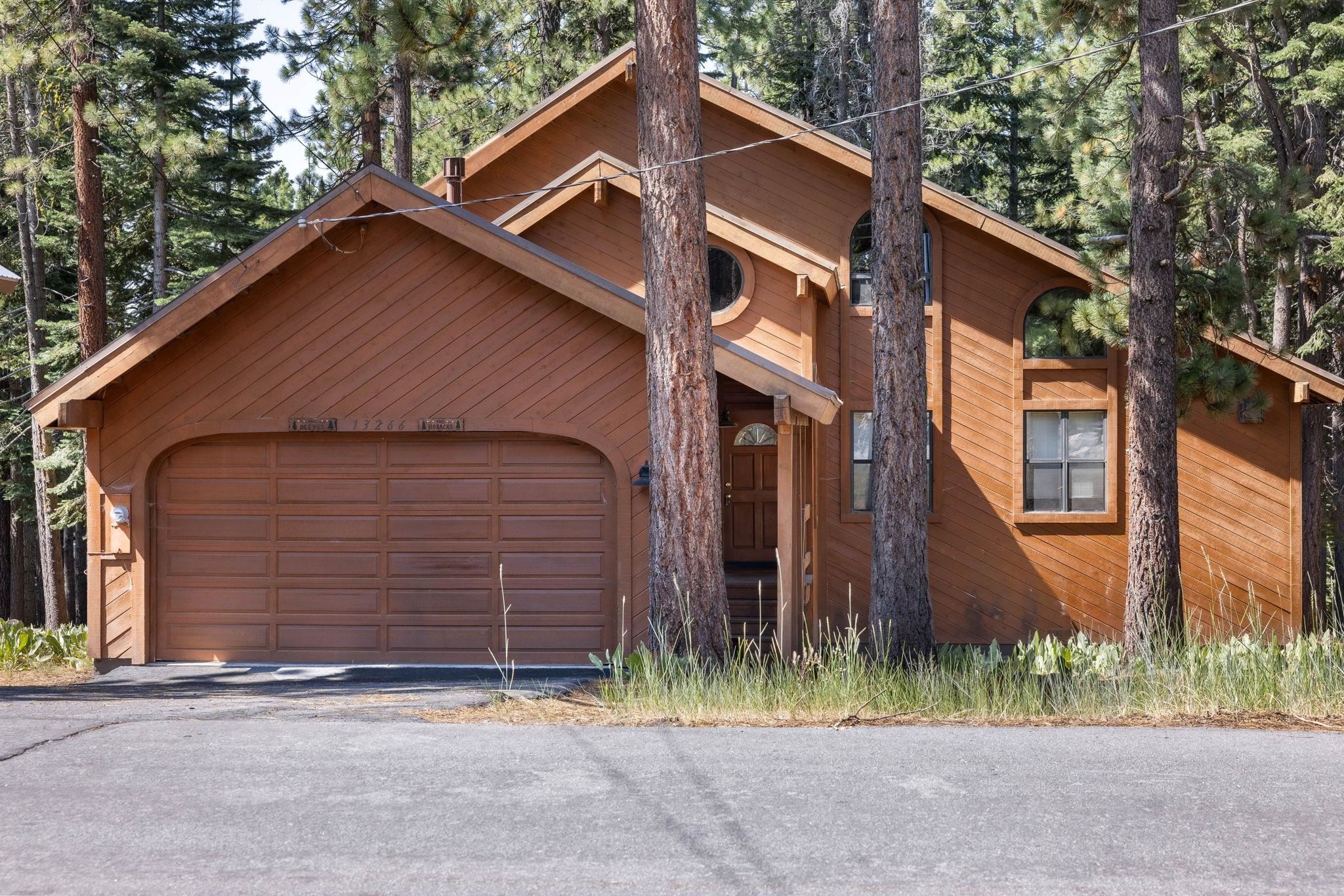 Wood-sided mountain home among pine trees, with a large garage and distinctive arched windows.