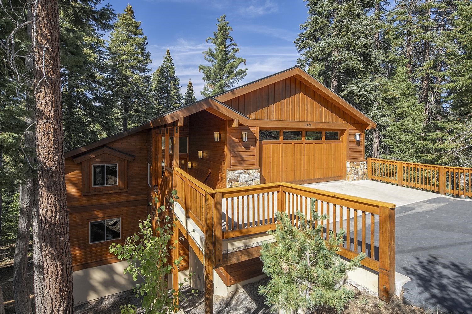 Wood-sided cabin-style home with a broad deck and driveway among tall evergreen trees.