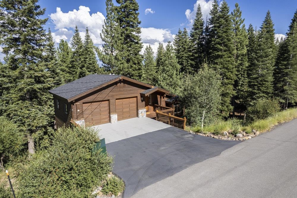 Wood-sided home with a two-car garage and deck surrounded by pine trees.