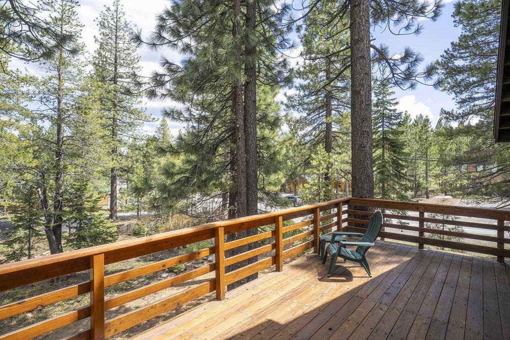 Wooden deck with green chairs overlooking tall pine trees.