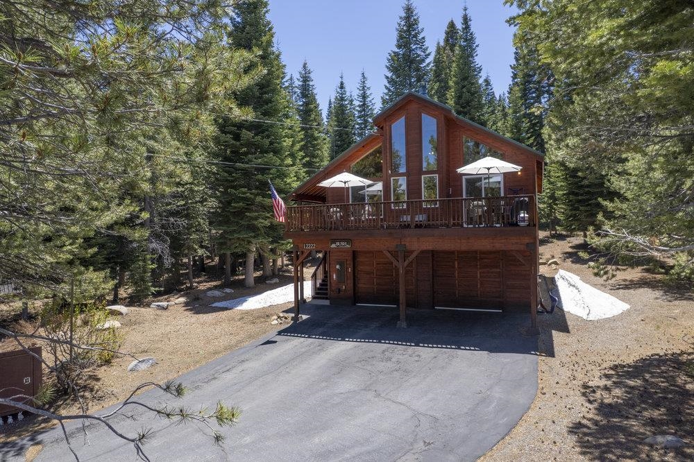 Wood cabin with a broad deck and garage beneath, surrounded by evergreen trees.